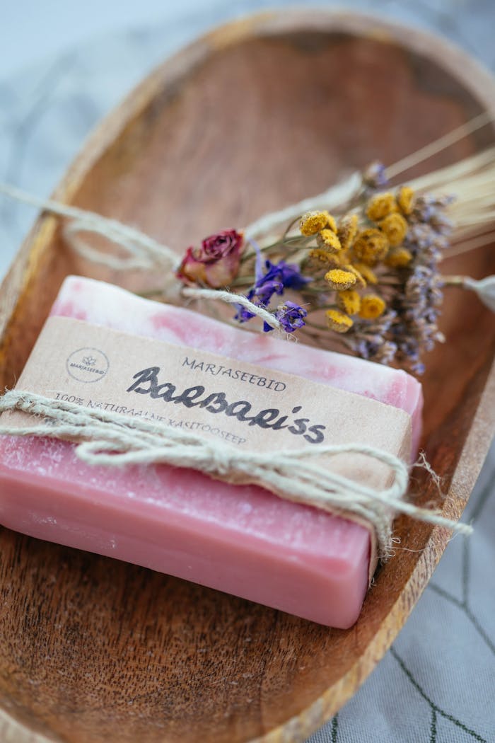 Pink artisanal bar soap with dried flowers in a wooden dish for an elegant touch.