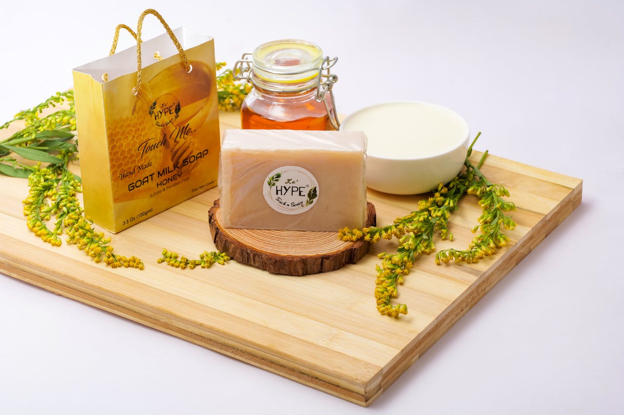 A natural soap display featuring goat milk soap, honey, and flowers on a wooden tray.